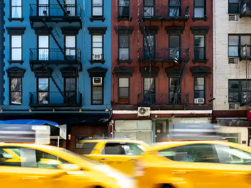 Blurry taxis in traffic in front of an apartment bulding.