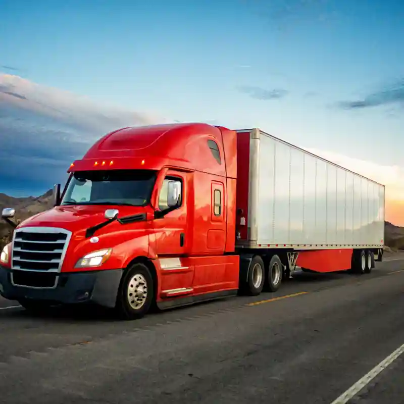 Red tractor trailer on the highway at dusk.